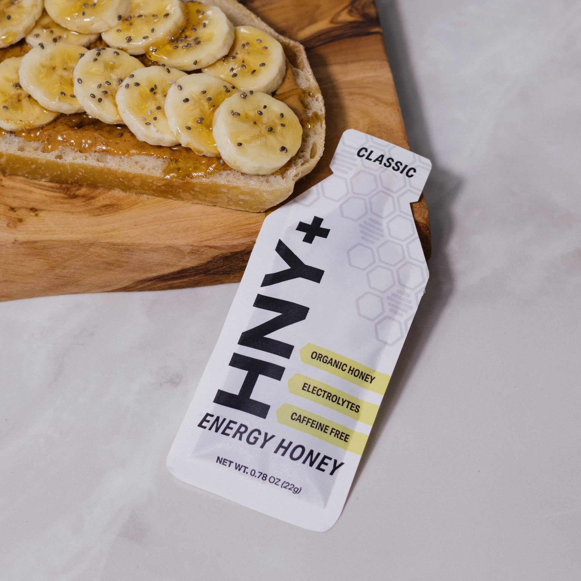 HNY+ energy honey packet with a slice of toast with bananas on a wooden board.